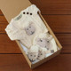 Sheply the Sheep Baby Gift Set featuring a cream-colored knitted sweater with sheep design, matching hat and booties with sheep faces, arranged in an open cardboard box on a wooden surface. Sheply the Sheep Baby Gift Set featuring a cream-colored knitted sweater with sheep design, matching hat and booties with sheep faces, arranged in an open cardboard box on a wooden surface.